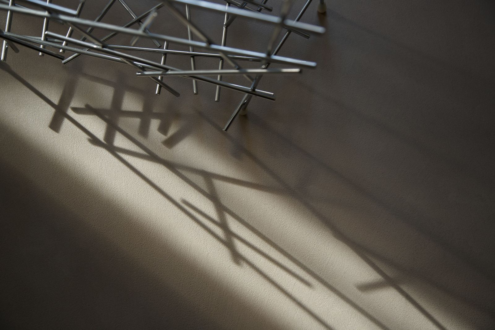 Superficie in cemento architettonico in luce radente, attraversata dalle ombre di una struttura metallica