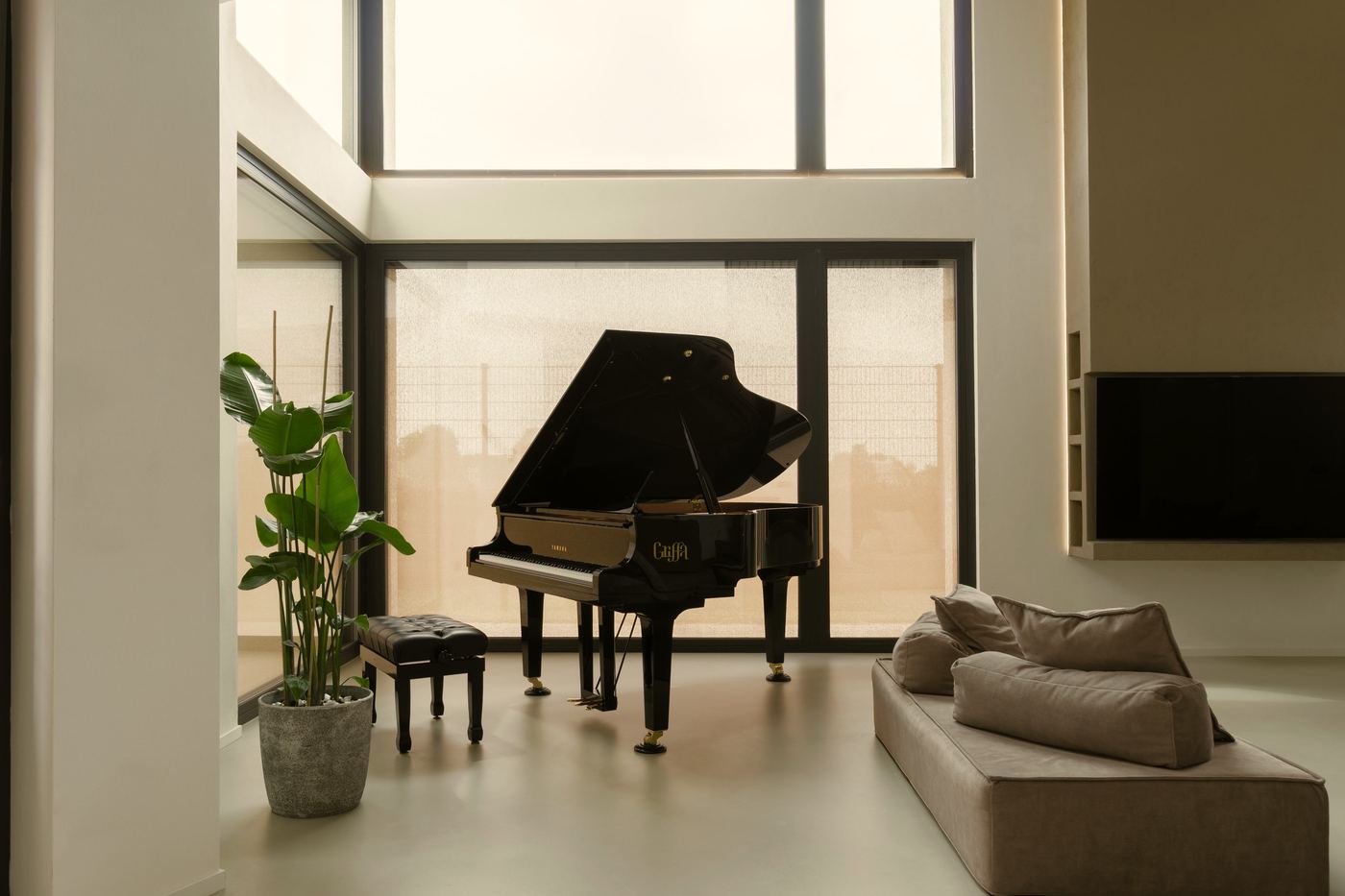 Zona giorno a doppia altezza con pavimento continuo in cemento architettonico e pianoforte a coda